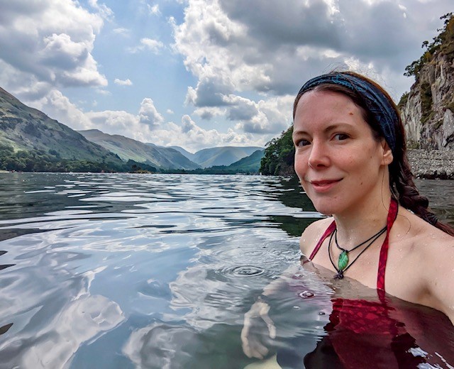 Headshot of Dee submerged in water with mountains and the sky in the background.