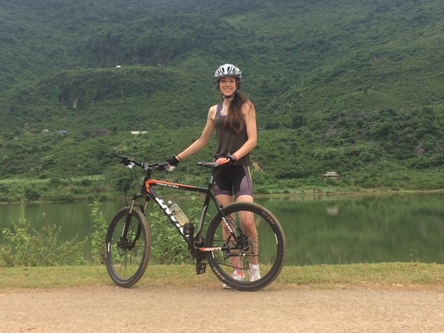 Emily holding a bike with green hills in the background.