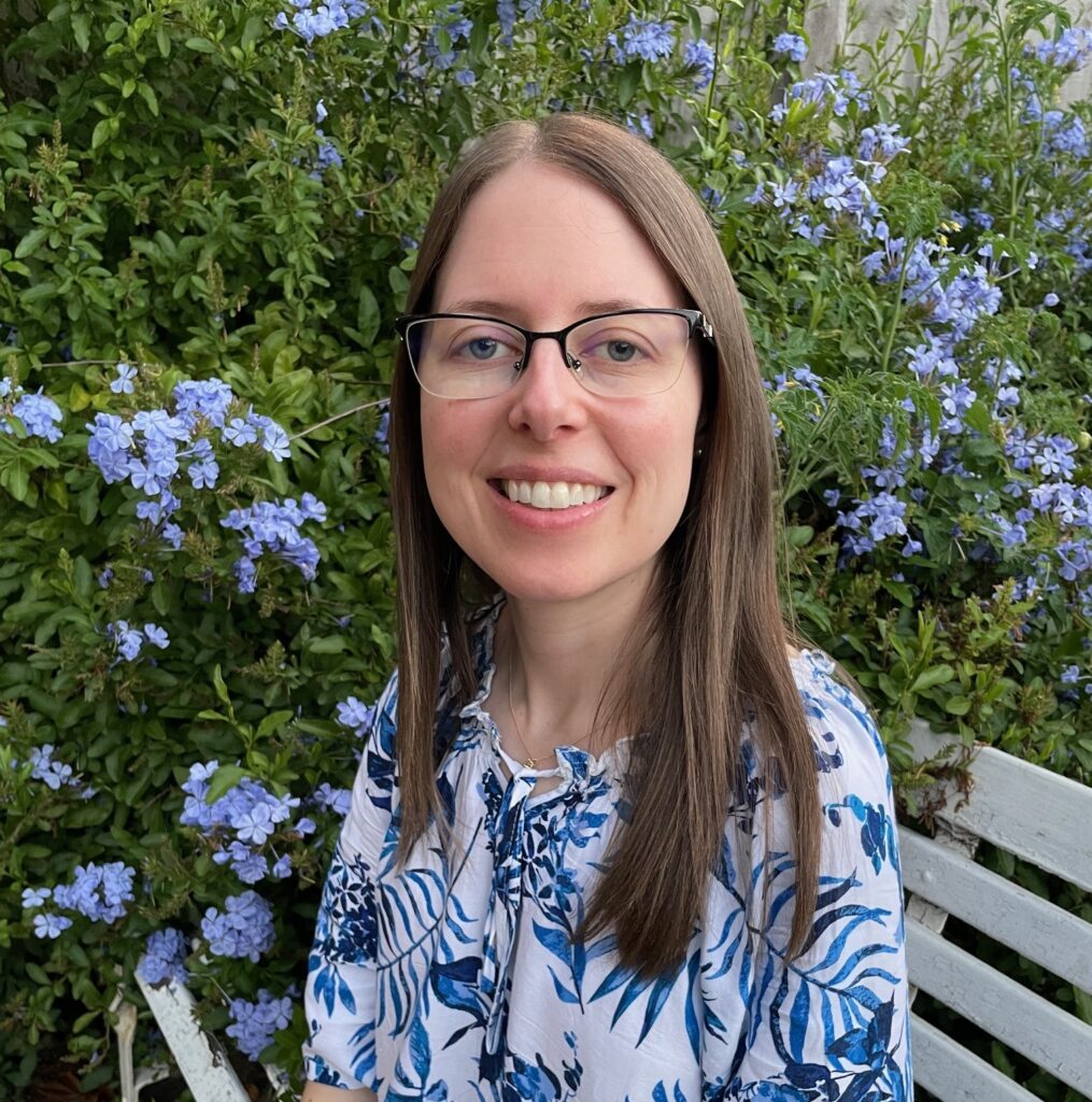 Head and shoulder photo of Catherine in front of a bush with lilac flowers,