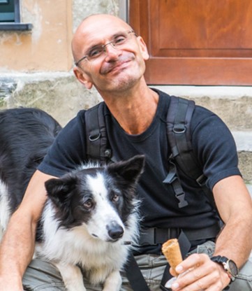Photo of Derek with a black and white dog on his lap.