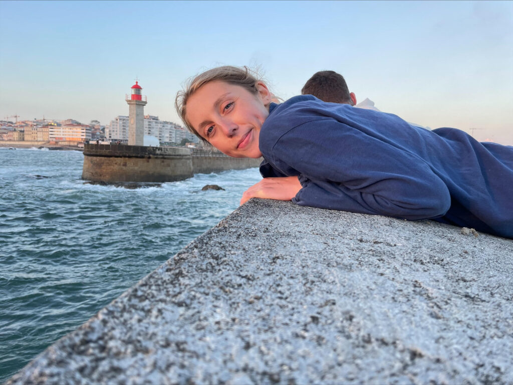 Photo of Charli with her chest leaning on a wall with a boat in the background.