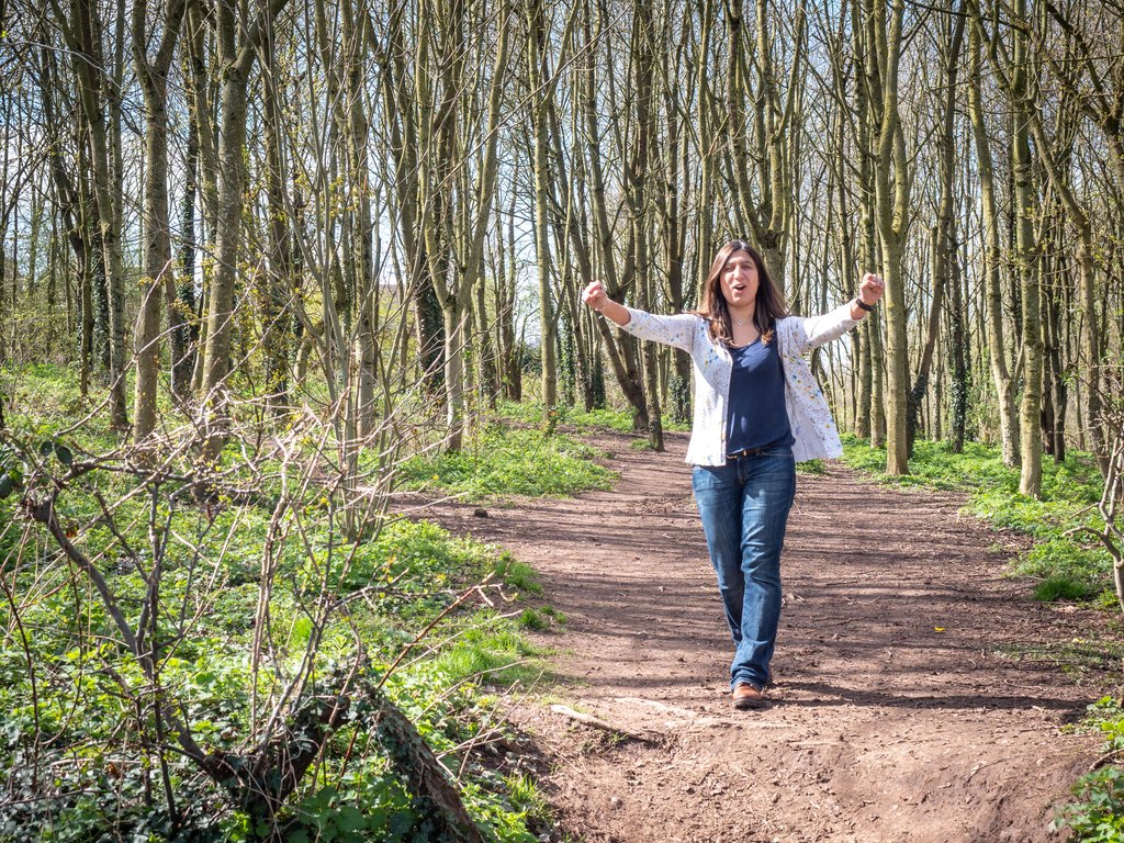Narinder walking a woodland path with her arms out in front of her.